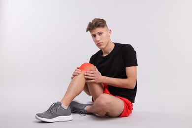 Young man suffering from pain in knee on light background