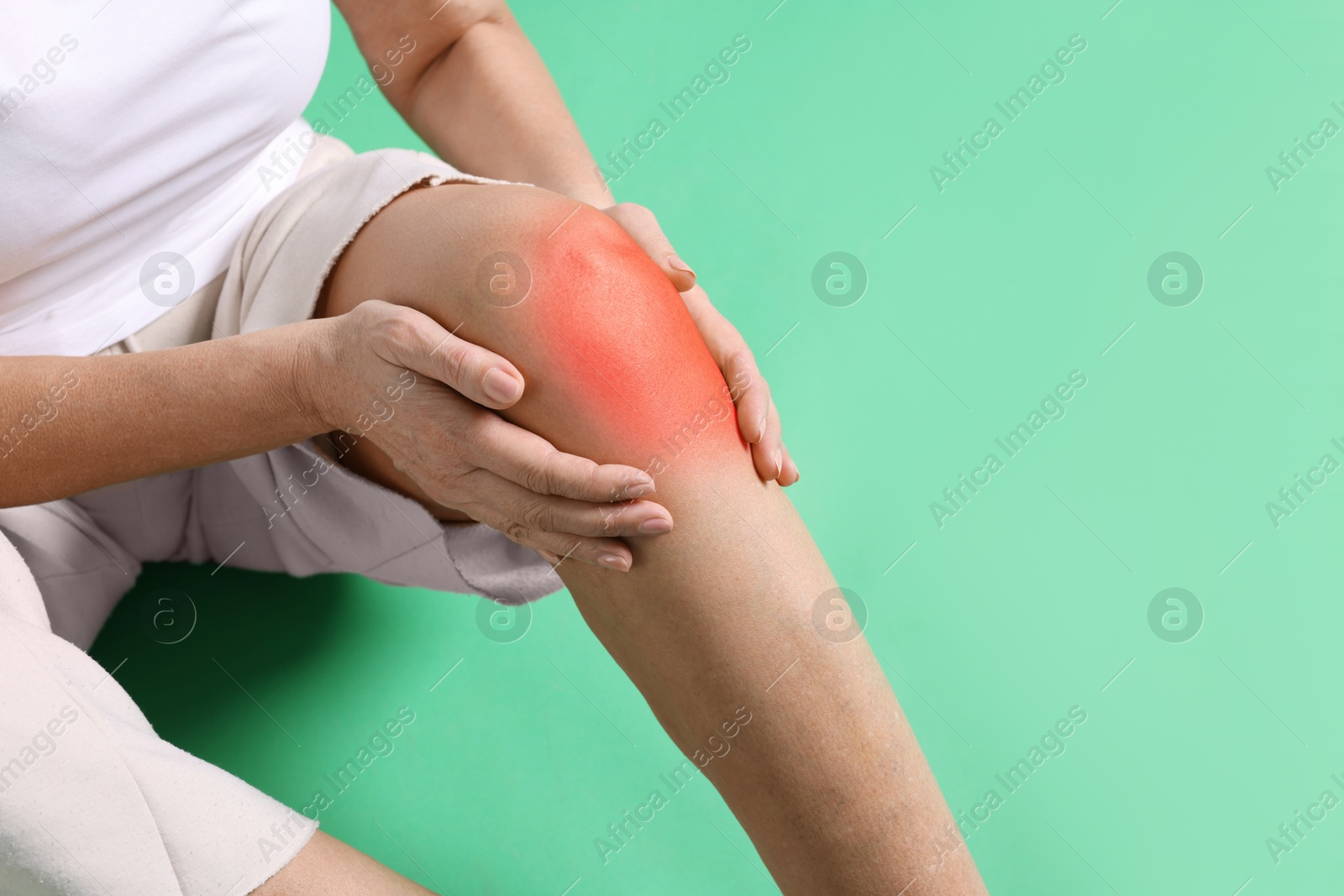 Image of Senior woman suffering from pain in knee on green background, closeup