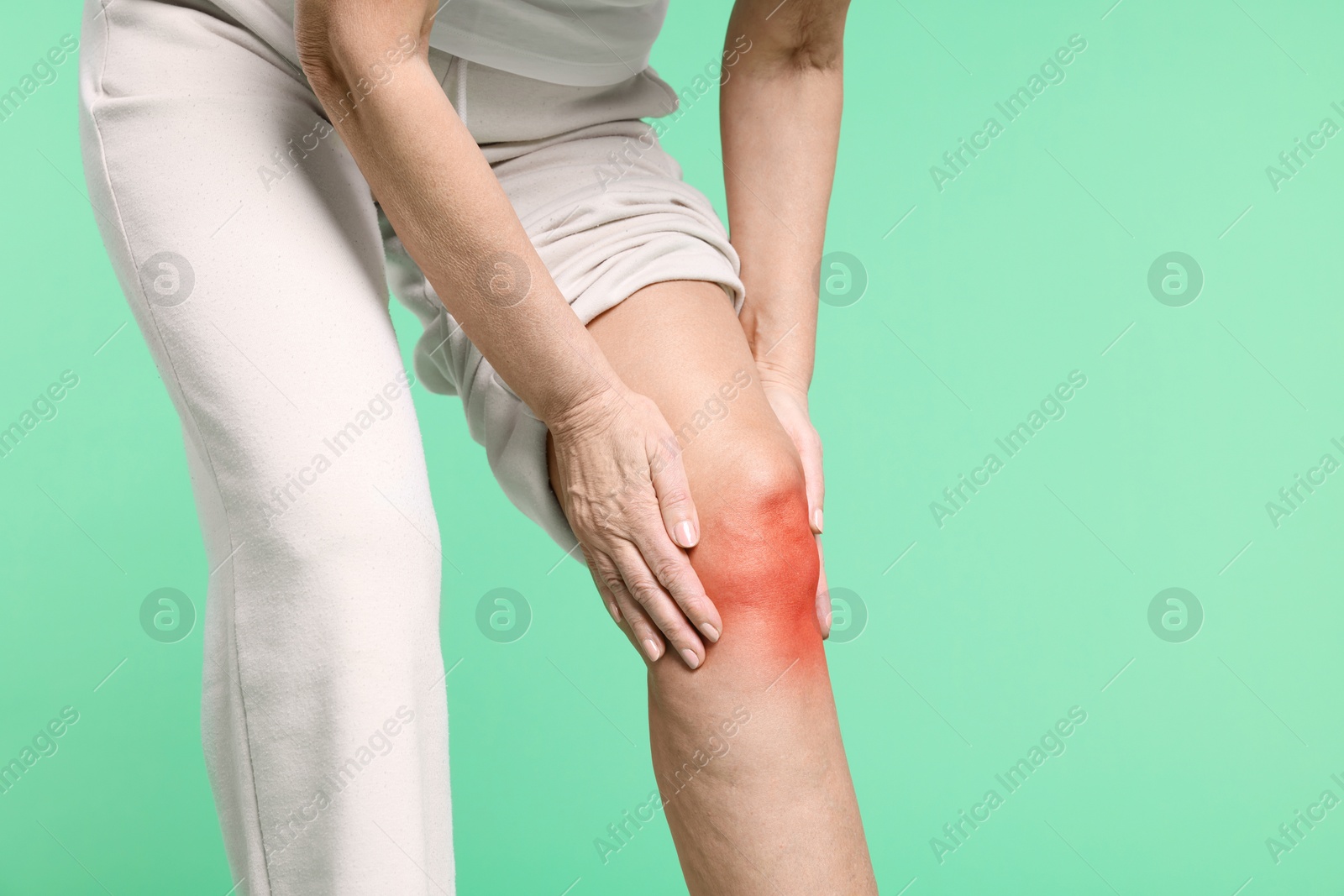 Image of Senior woman suffering from pain in knee on green background, closeup