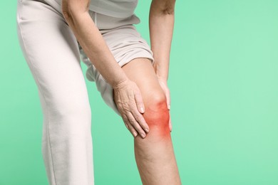 Image of Senior woman suffering from pain in knee on green background, closeup