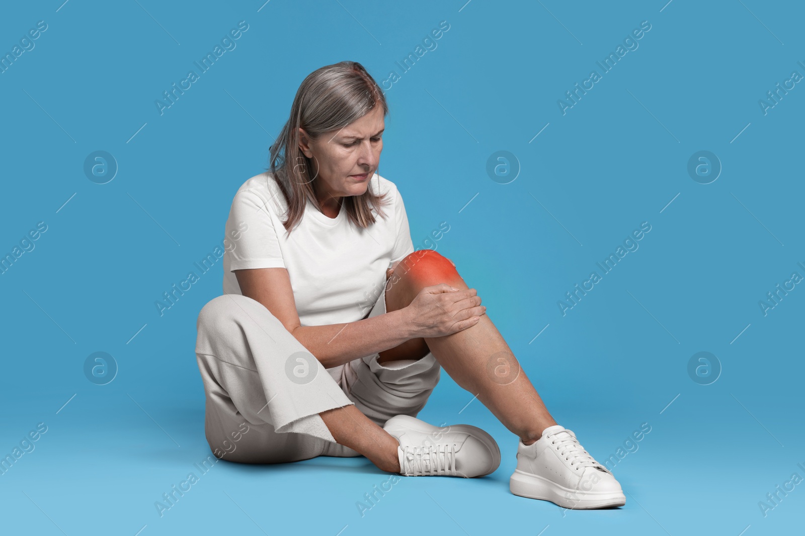 Image of Senior woman suffering from pain in knee on light blue background