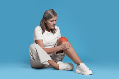 Image of Senior woman suffering from pain in knee on light blue background