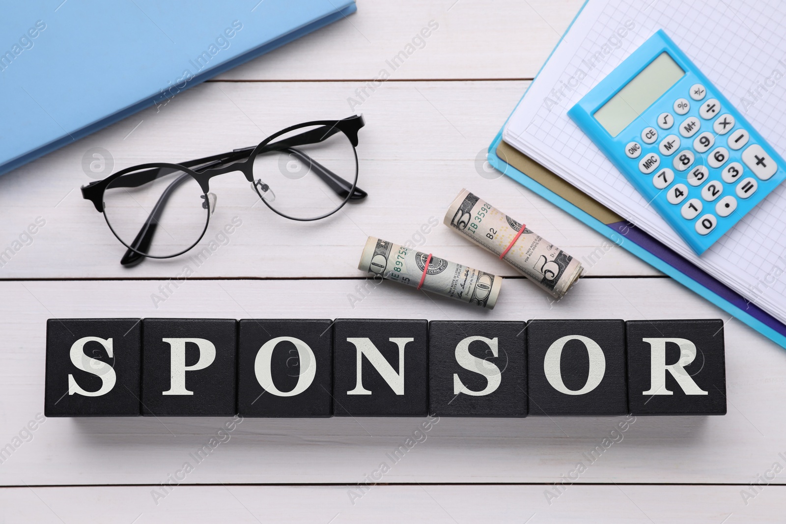 Image of Word Sponsor made of black cubes with letters, dollar banknotes, eyeglasses, notebooks and calculator on white wooden table, top view