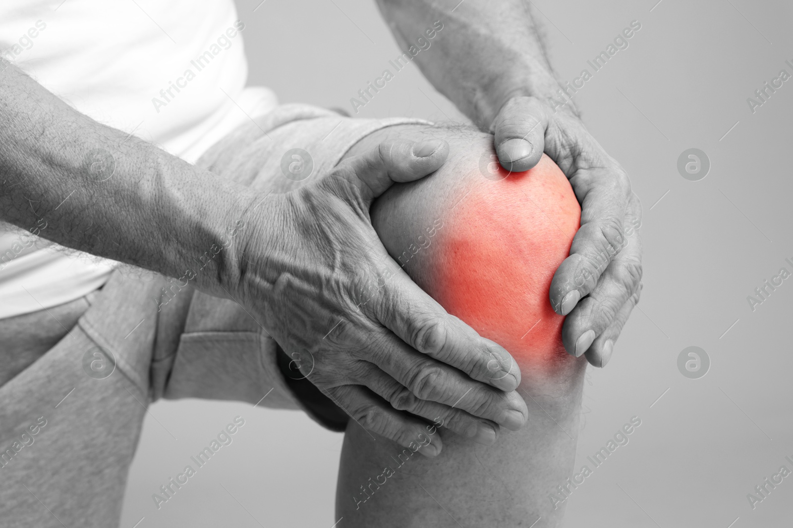 Image of Senior man suffering from pain in knee, closeup. Black-and-white effect with red color accent