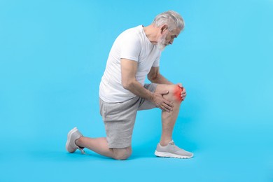 Image of Senior man suffering from pain in knee on light blue background