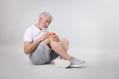 Senior man suffering from pain in knee on light grey background