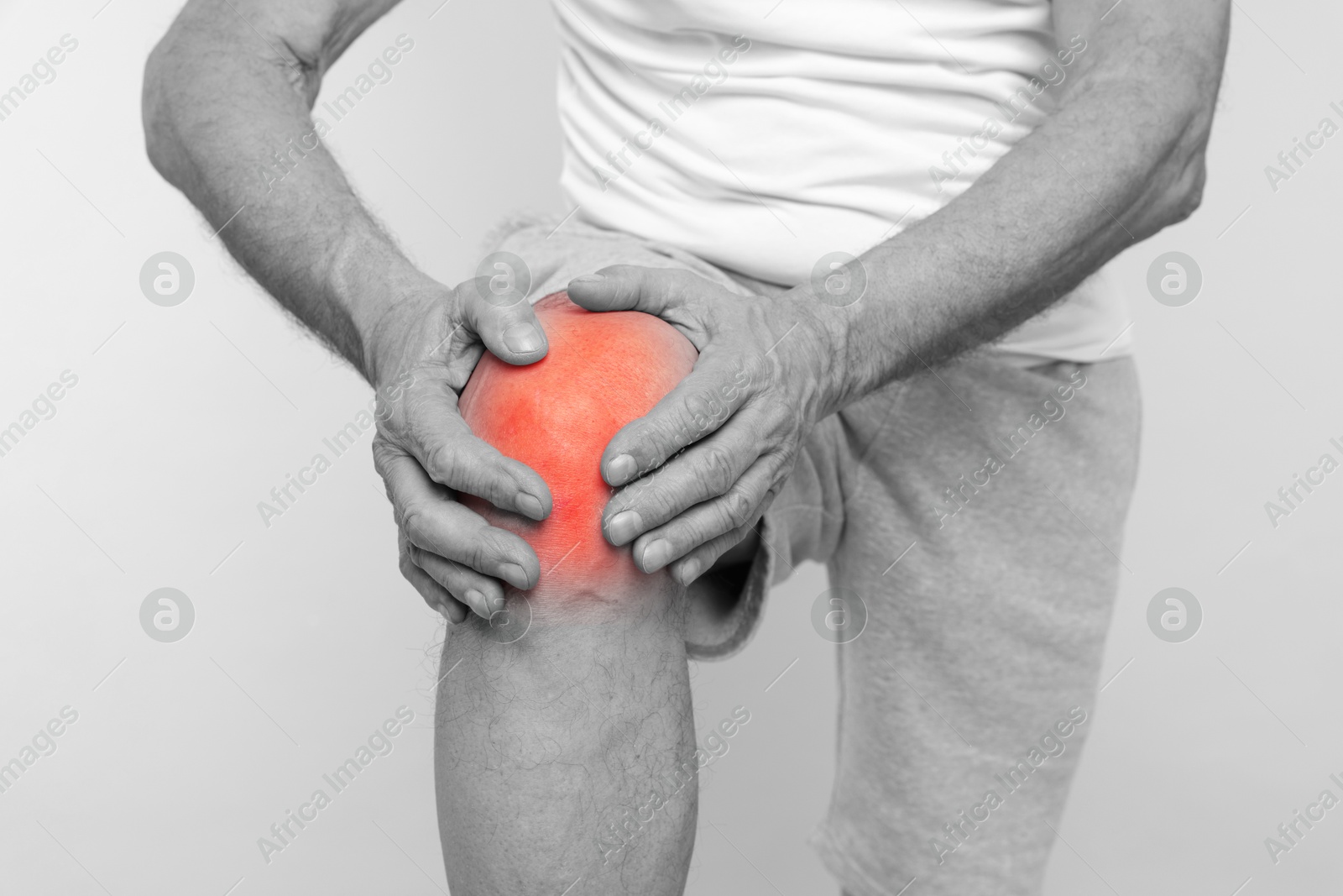 Image of Senior man suffering from pain in knee, closeup. Black-and-white effect with red color accent