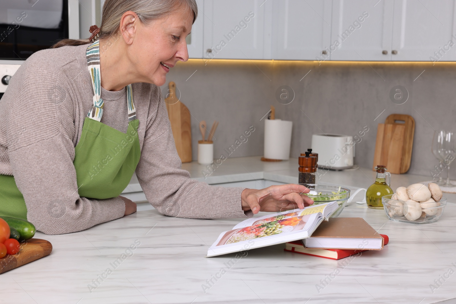 Photo of Happy woman with recipe book at table in kitchen