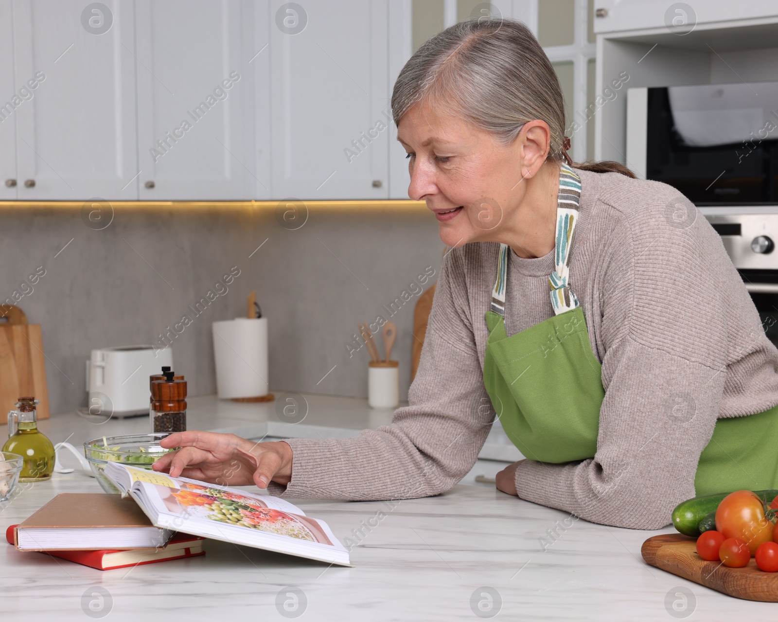 Photo of Happy woman with recipe book at table in kitchen