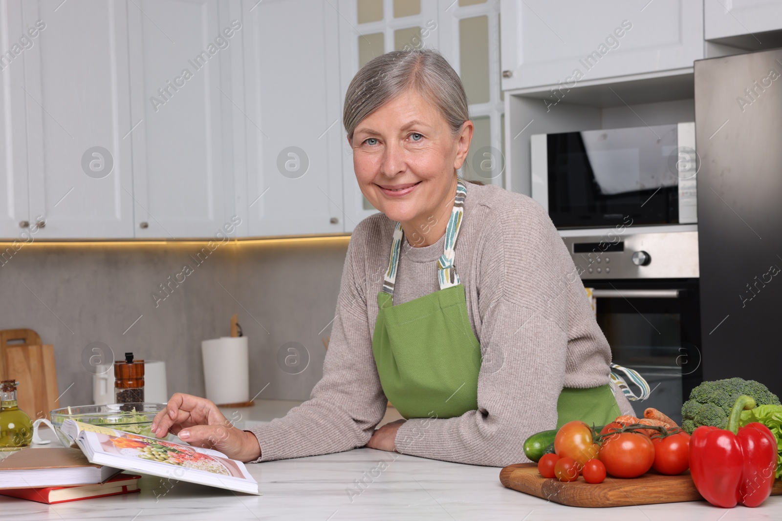 Photo of Happy woman with recipe book at table in kitchen