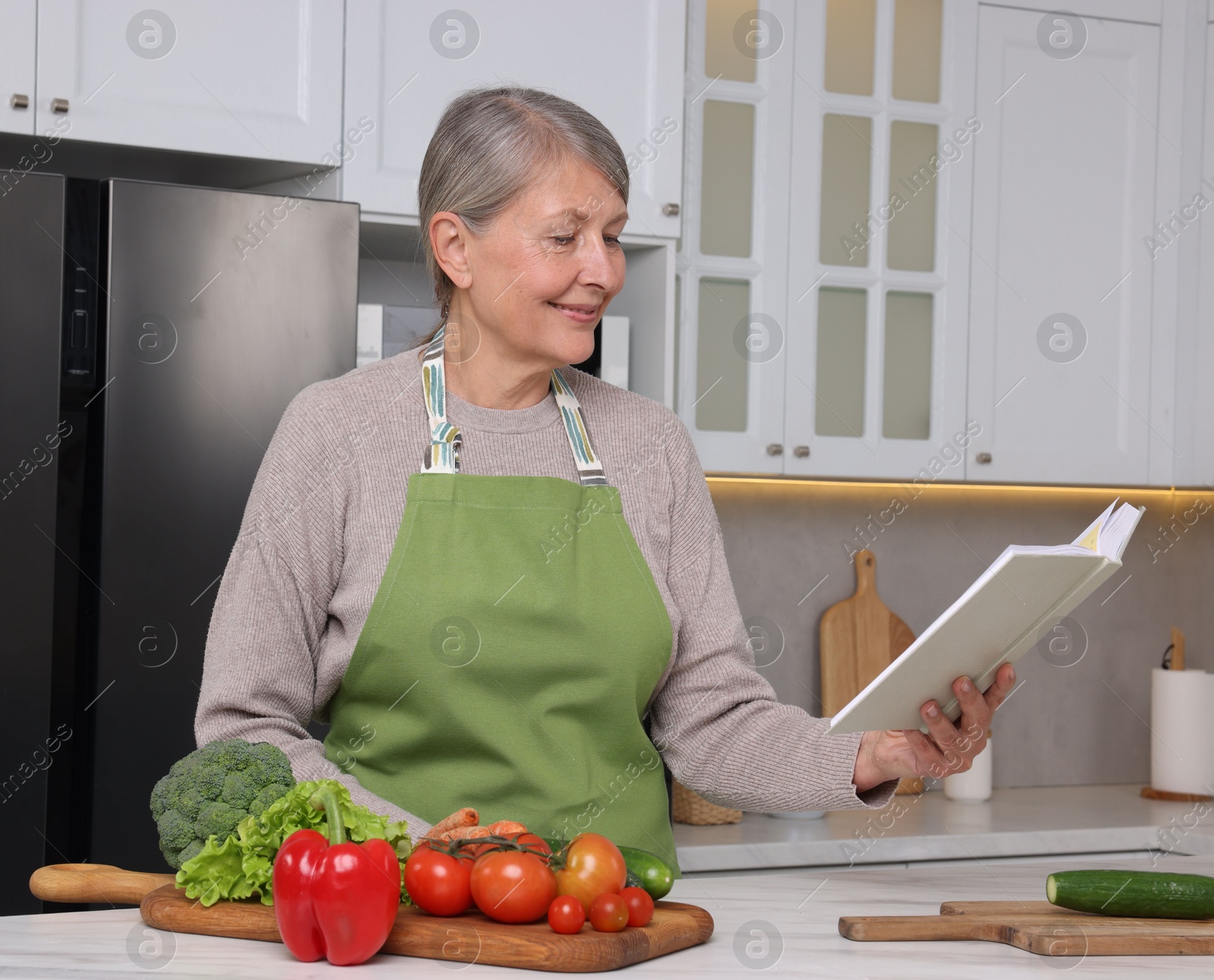 Photo of Happy woman with recipe book at table in kitchen