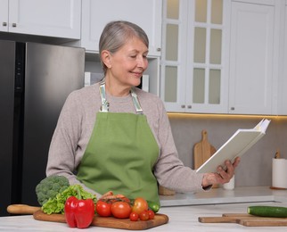 Happy woman with recipe book at table in kitchen