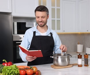 Happy man cooking by recipe book in kitchen