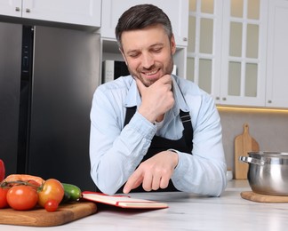 Photo of Adult man reading recipe book at white marble table in kitchen