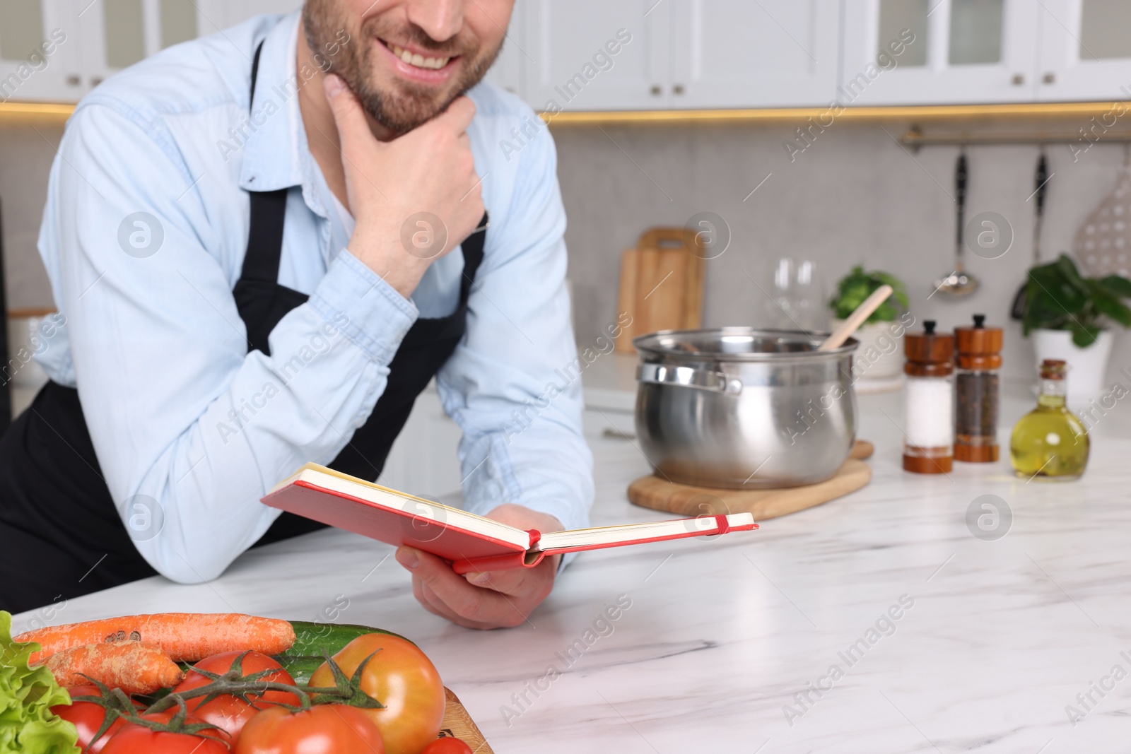 Photo of Man with recipe book at white marble table in kitchen, closeup