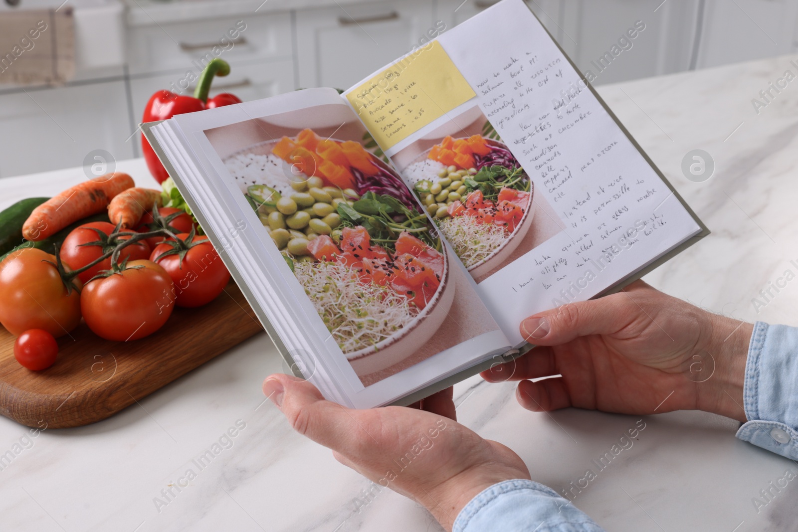 Photo of Man with recipe book at white marble table in kitchen, closeup