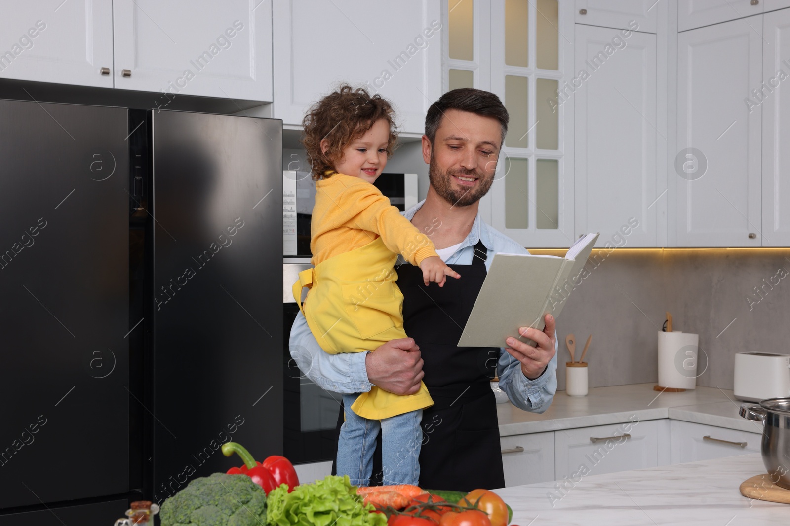 Photo of Cute little girl and her father with recipe book cooking in kitchen