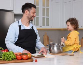 Cute little girl and her father with recipe book cooking in kitchen