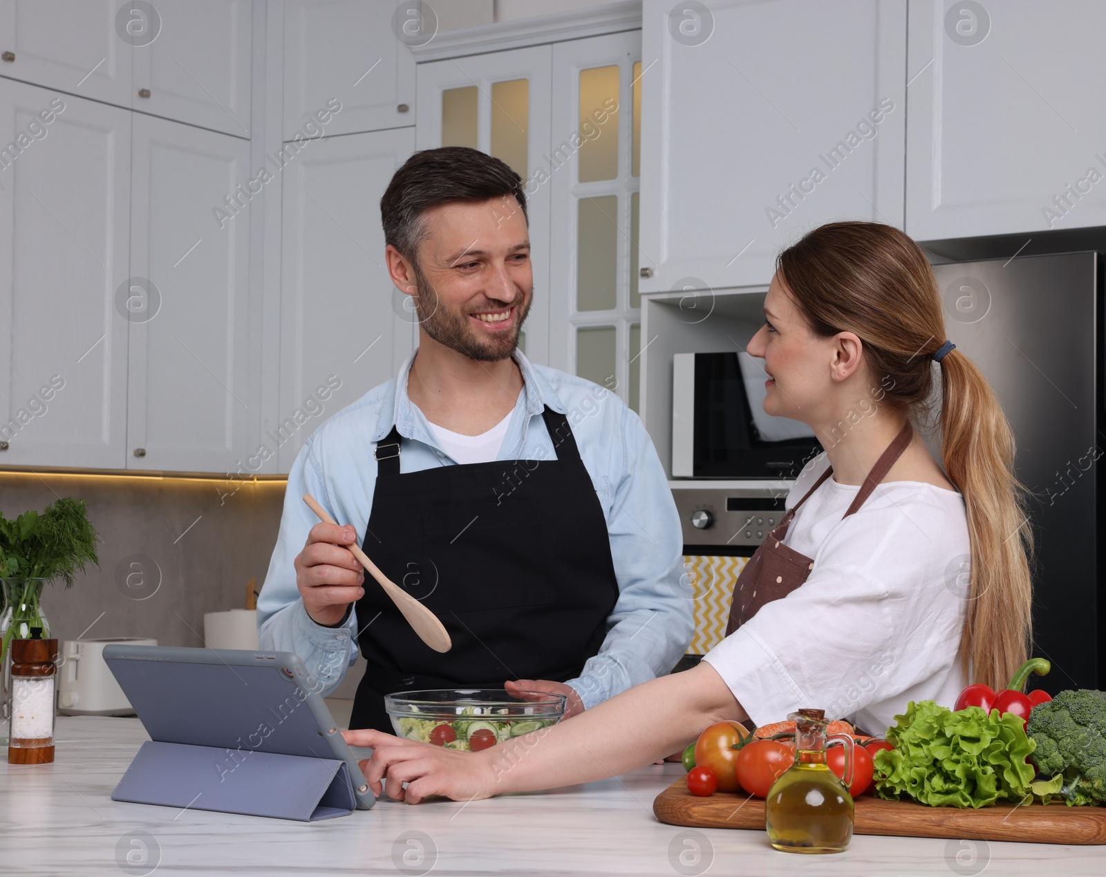 Photo of Happy couple reading recipe on tablet while cooking in kitchen. Online culinary book