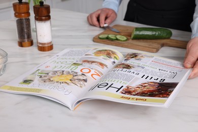 Photo of Man reading recipe in culinary magazine while cooking at home, closeup