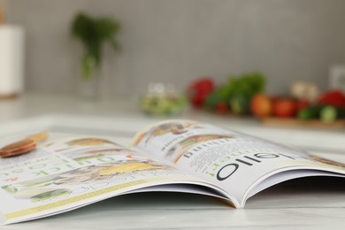 Photo of Open culinary magazine on white table in kitchen, closeup. Space for text