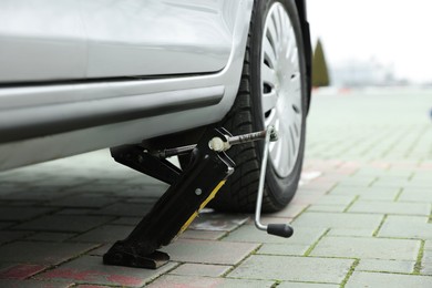 Photo of Car lifted by scissor jack on roadside outdoors