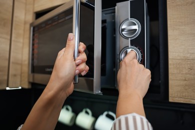 Woman turning on microwave at home, closeup