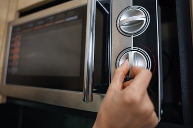 Photo of Woman turning on microwave at home, closeup