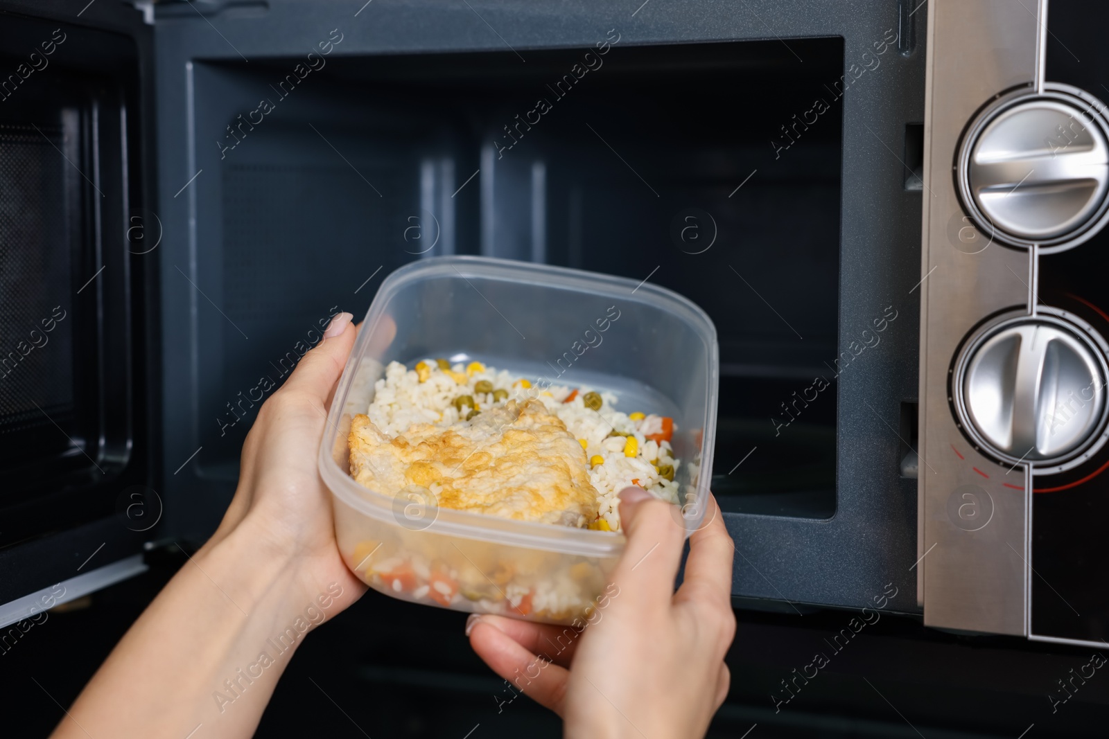 Photo of Woman putting container with lunch into microwave indoors, closeup