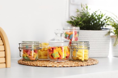 Photo of Tasty gummy candies in glass jars on white table