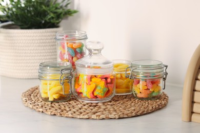 Photo of Tasty gummy candies in glass jars on white table