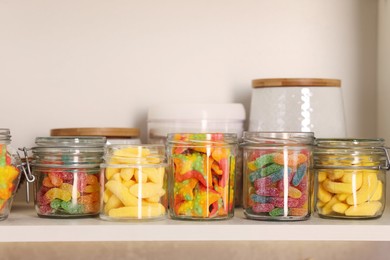 Photo of Tasty gummy candies in jars on shelf