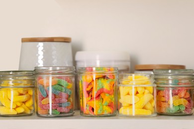 Photo of Tasty gummy candies in jars on shelf