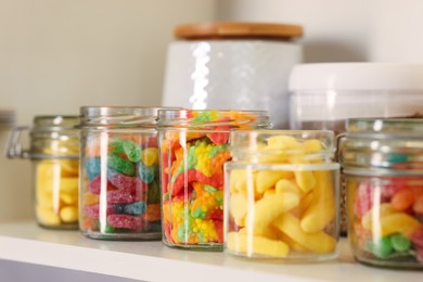 Photo of Tasty gummy candies in jars on shelf, closeup