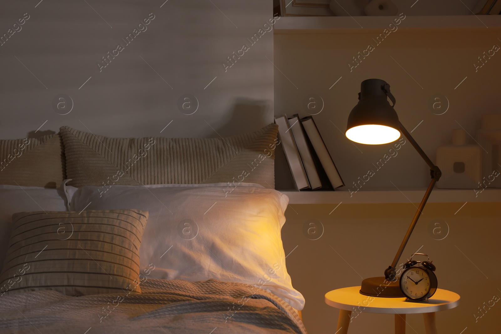 Photo of Glowing night lamp and alarm clock on bedside table indoors