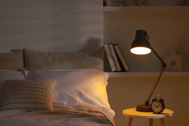 Photo of Glowing night lamp and alarm clock on bedside table indoors