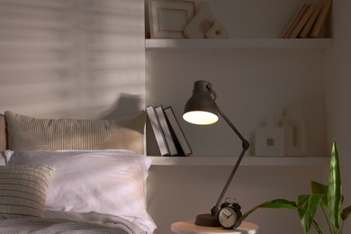 Photo of Glowing night lamp and alarm clock on bedside table indoors