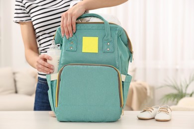 Mother packing baby's stuff into bag at white table, closeup