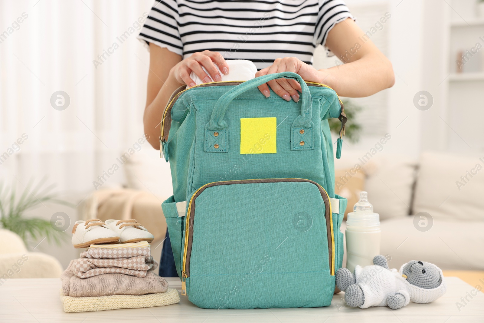 Photo of Mother packing baby's stuff into bag at white table, closeup