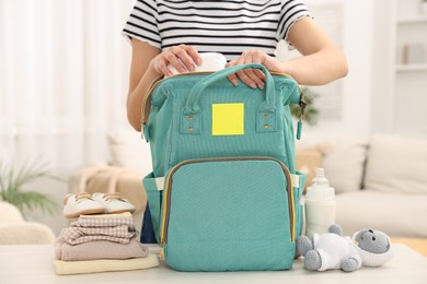 Photo of Mother packing baby's stuff into bag at white table, closeup