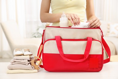 Photo of Mother packing baby's stuff into bag at white table, closeup