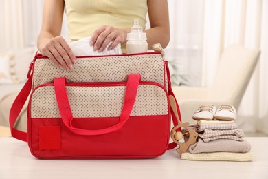 Photo of Mother packing baby's stuff into bag at white table, closeup