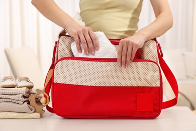 Mother packing baby's stuff into bag at white table, closeup