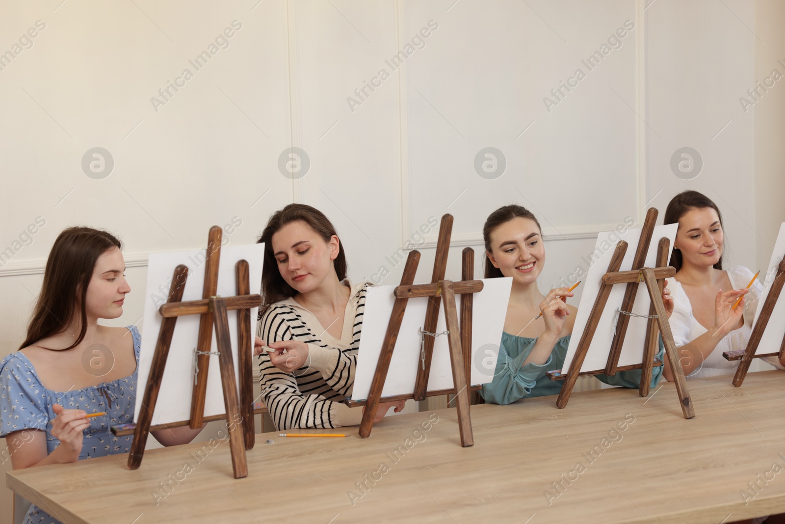 Photo of Group of women with easels learning to draw at wooden table in class