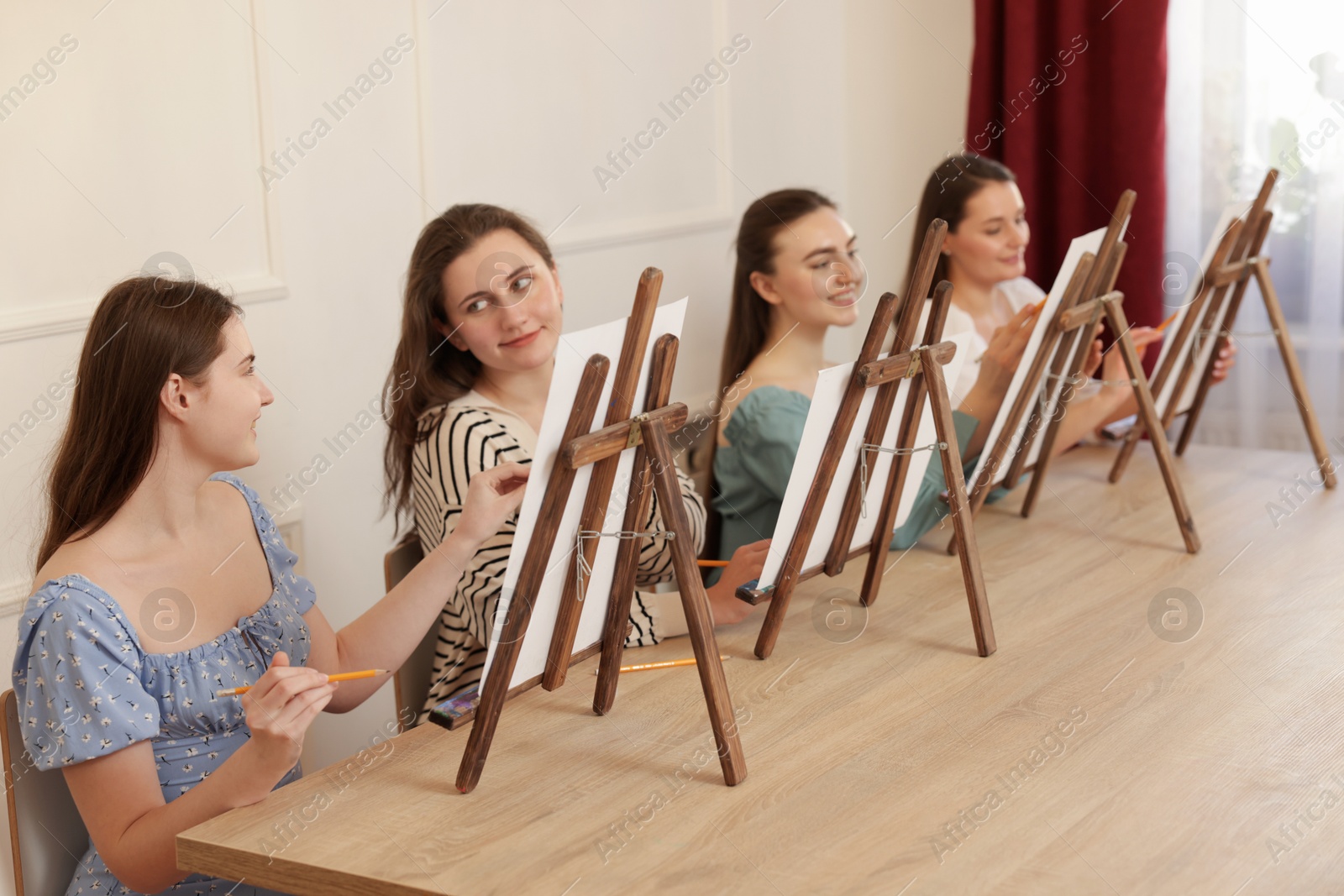 Photo of Group of women with easels learning to draw at wooden table in class