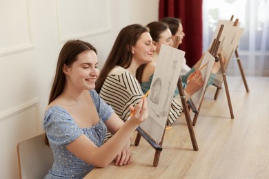 Photo of Group of women with easels learning to draw at wooden table in class