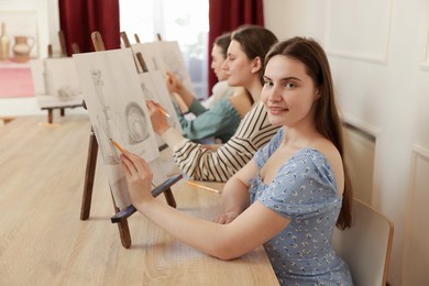 Group of women with easels learning to draw at wooden table in class