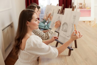 Photo of Group of women with easels learning to draw at wooden table in class