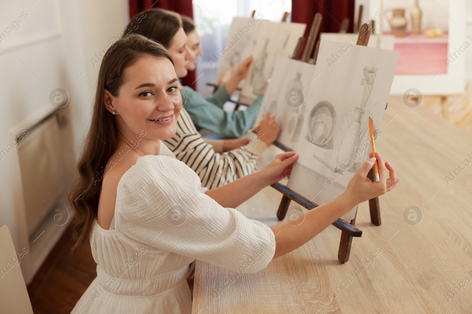 Photo of Group of women with easels learning to draw at wooden table in class