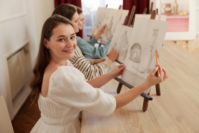 Group of women with easels learning to draw at wooden table in class